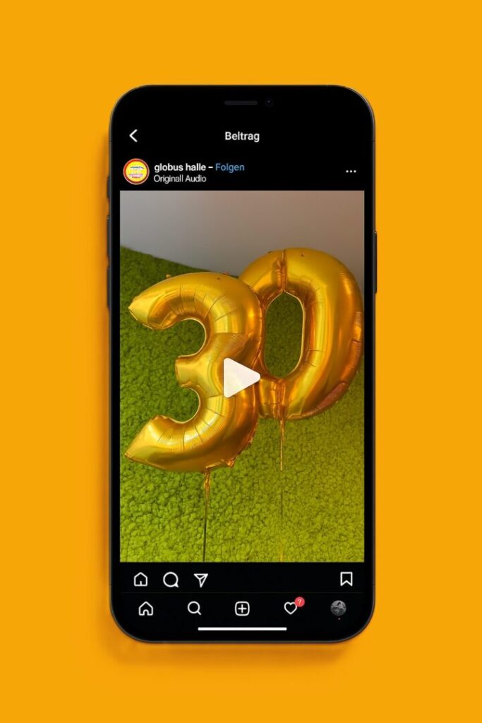 Instagram post on a phone showing gold foil balloons forming the number 30 against a green lawn, with a play button overlay on the image.